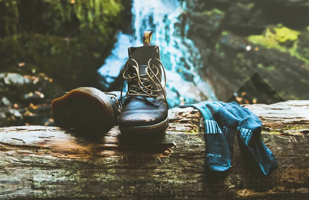 braune Schuhe und blaue Socken auf einem Baumstamm vor einem Wasserfall