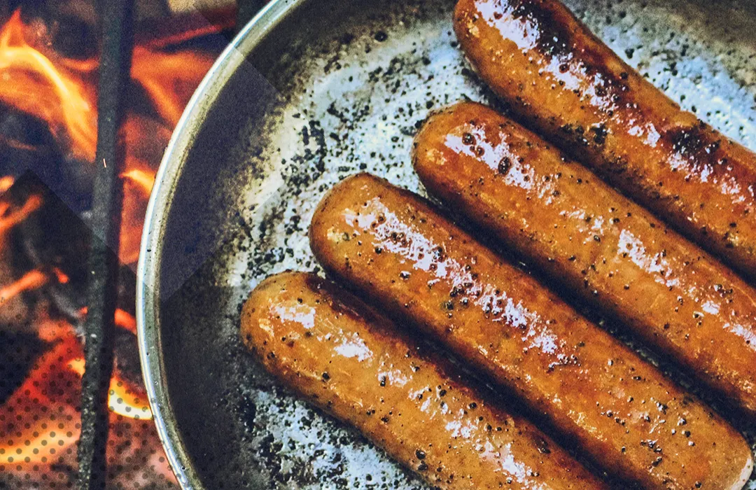 Würstchen in einer Pfanne über offenem Feuer